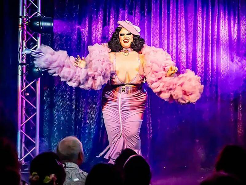 Image shows Katie performing a burlesque show, wearing a pink dress, feather boa, and hat.